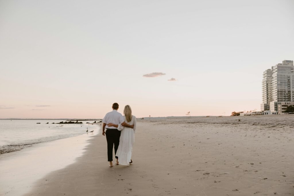 A couple walks arm in arm along a serene beach at sunset, conveying romance and tranquility.